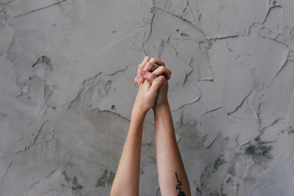 Close-up of two hands holding against a textured gray wall, symbolizing unity.
