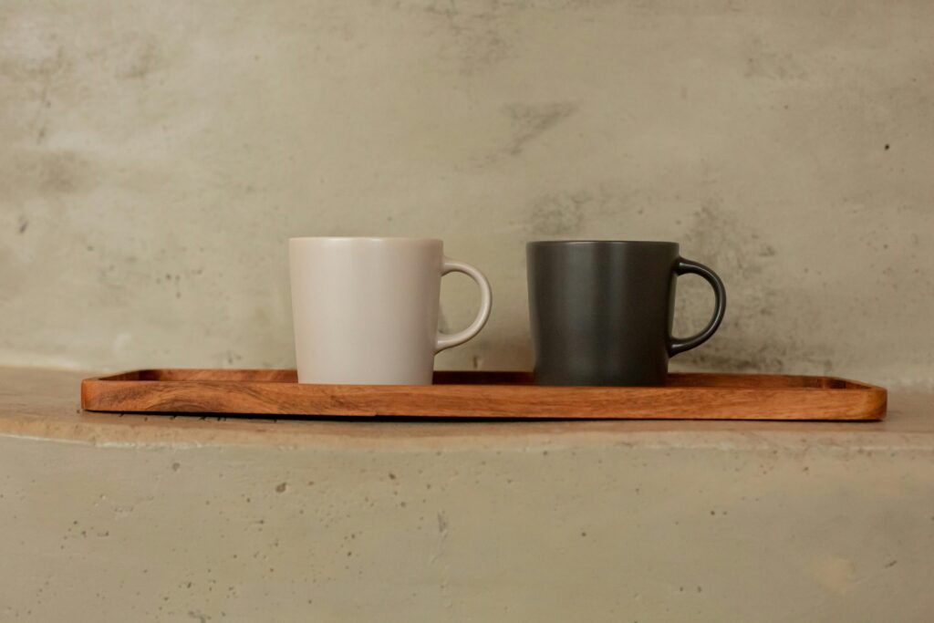 Two ceramic mugs displayed on a wooden tray with a concrete backdrop.